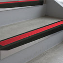 Satin Black deep-riser square-edge aluminium stair nosing fitted along two bare concrete steps, 62mm tread plate and 56mm front face, with a Red anti-slip insert running the full width of each step