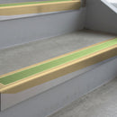 Satin Bronze deep-riser square-edge aluminium stair nosing fitted along two bare concrete steps, 62mm tread plate and 56mm front face, with a Apple Green anti-slip insert running the full width of each step