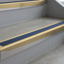 Satin Bronze deep-riser square-edge aluminium stair nosing fitted along two bare concrete steps, 62mm tread plate and 56mm front face, with a Blue anti-slip insert running the full width of each step