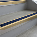 Satin Bronze deep-riser square-edge aluminium stair nosing fitted along two bare concrete steps, 62mm tread plate and 56mm front face, with a Dark Blue anti-slip insert running the full width of each step
