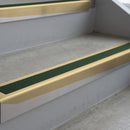 Satin Bronze deep-riser square-edge aluminium stair nosing fitted along two bare concrete steps, 62mm tread plate and 56mm front face, with a Dark Green anti-slip insert running the full width of each step