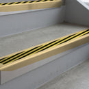Satin Bronze deep-riser square-edge aluminium stair nosing fitted along two bare concrete steps, 62mm tread plate and 56mm front face, with a Hazard anti-slip insert running the full width of each step
