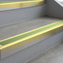 Satin Gold deep-riser square-edge aluminium stair nosing fitted along two bare concrete steps, 62mm tread plate and 56mm front face, with a Apple Green anti-slip insert running the full width of each step