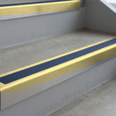 Satin Gold deep-riser square-edge aluminium stair nosing fitted along two bare concrete steps, 62mm tread plate and 56mm front face, with a Blue anti-slip insert running the full width of each step