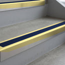 Satin Gold deep-riser square-edge aluminium stair nosing fitted along two bare concrete steps, 62mm tread plate and 56mm front face, with a Dark Blue anti-slip insert running the full width of each step