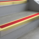 Satin Gold deep-riser square-edge aluminium stair nosing fitted along two bare concrete steps, 62mm tread plate and 56mm front face, with a Red anti-slip insert running the full width of each step