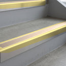 Satin Gold deep-riser square-edge aluminium stair nosing fitted along two bare concrete steps, 62mm tread plate and 56mm front face, with a Sahara anti-slip insert running the full width of each step