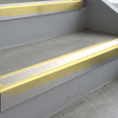 Satin Gold deep-riser square-edge aluminium stair nosing fitted along two bare concrete steps, 62mm tread plate and 56mm front face, with a White anti-slip insert running the full width of each step