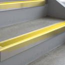 Satin Gold deep-riser square-edge aluminium stair nosing fitted along two bare concrete steps, 62mm tread plate and 56mm front face, with a Yellow anti-slip insert running the full width of each step