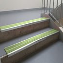 Bright Polished aluminium stair nosing fitted along two concrete steps in an office stairwell, with twin Apple Green anti-slip inserts running the full width of each step
