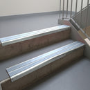 Bright Polished aluminium stair nosing fitted along two concrete steps in an office stairwell, with twin Aura anti-slip inserts running the full width of each step