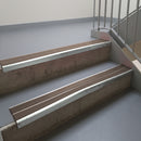 Bright Polished aluminium stair nosing fitted along two concrete steps in an office stairwell, with twin Brown anti-slip inserts running the full width of each step