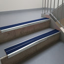 Bright Polished aluminium stair nosing fitted along two concrete steps in an office stairwell, with twin Dark Blue anti-slip inserts running the full width of each step
