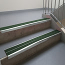 Bright Polished aluminium stair nosing fitted along two concrete steps in an office stairwell, with twin Dark Green anti-slip inserts running the full width of each step