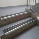 Bright Polished aluminium stair nosing fitted along two concrete steps in an office stairwell, with twin Dark Grey anti-slip inserts running the full width of each step