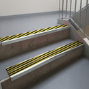 Bright Polished aluminium stair nosing fitted along two concrete steps in an office stairwell, with twin Hazard black and yellow anti-slip inserts running the full width of each step