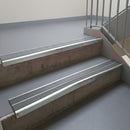 Bright Polished aluminium stair nosing fitted along two concrete steps in an office stairwell, with twin Mid Grey anti-slip inserts running the full width of each step