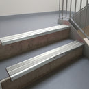 Bright Polished aluminium stair nosing fitted along two concrete steps in an office stairwell, with twin Oyster anti-slip inserts running the full width of each step
