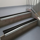 Bright Polished aluminium stair nosing fitted along two concrete steps in an office stairwell, with twin Premium Black anti-slip inserts running the full width of each step