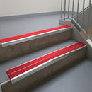 Bright Polished aluminium stair nosing fitted along two concrete steps in an office stairwell, with twin Red anti-slip inserts running the full width of each step