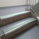 Bright Polished aluminium stair nosing fitted along two concrete steps in an office stairwell, with twin Sage Green anti-slip inserts running the full width of each step