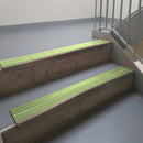 Dark Bronze aluminium stair nosing fitted along two concrete steps in an office stairwell, with twin Apple Green anti-slip inserts running the full width of each step