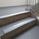 Dark Bronze aluminium stair nosing fitted along two concrete steps in an office stairwell, with twin Aura anti-slip inserts running the full width of each step