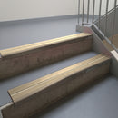 Dark Bronze aluminium stair nosing fitted along two concrete steps in an office stairwell, with twin Beige anti-slip inserts running the full width of each step