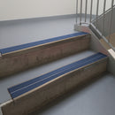Dark Bronze aluminium stair nosing fitted along two concrete steps in an office stairwell, with twin Blue anti-slip inserts running the full width of each step