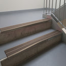 Dark Bronze aluminium stair nosing fitted along two concrete steps in an office stairwell, with twin Brown anti-slip inserts running the full width of each step
