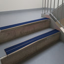 Dark Bronze aluminium stair nosing fitted along two concrete steps in an office stairwell, with twin Dark Blue anti-slip inserts running the full width of each step