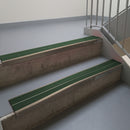 Dark Bronze aluminium stair nosing fitted along two concrete steps in an office stairwell, with twin Dark Green anti-slip inserts running the full width of each step