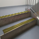 Dark Bronze aluminium stair nosing fitted along two concrete steps in an office stairwell, with twin Hazard black and yellow anti-slip inserts running the full width of each step