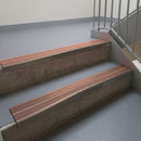 Dark Bronze aluminium stair nosing fitted along two concrete steps in an office stairwell, with twin Mid Brown anti-slip inserts running the full width of each step