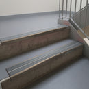 Dark Bronze aluminium stair nosing fitted along two concrete steps in an office stairwell, with twin Mid Grey anti-slip inserts running the full width of each step