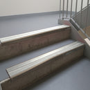 Dark Bronze aluminium stair nosing fitted along two concrete steps in an office stairwell, with twin Oyster anti-slip inserts running the full width of each step