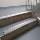 Dark Bronze aluminium stair nosing fitted along two concrete steps in an office stairwell, with twin Polar Grey anti-slip inserts running the full width of each step