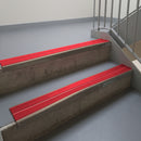 Dark Bronze aluminium stair nosing fitted along two concrete steps in an office stairwell, with twin Red anti-slip inserts running the full width of each step