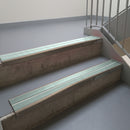 Dark Bronze aluminium stair nosing fitted along two concrete steps in an office stairwell, with twin Sage Green anti-slip inserts running the full width of each step