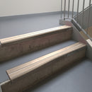 Dark Bronze aluminium stair nosing fitted along two concrete steps in an office stairwell, with twin Sahara anti-slip inserts running the full width of each step