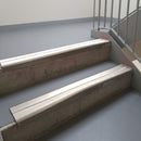 Dark Bronze aluminium stair nosing fitted along two concrete steps in an office stairwell, with twin White anti-slip inserts running the full width of each step