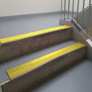 Dark Bronze aluminium stair nosing fitted along two concrete steps in an office stairwell, with twin Yellow anti-slip inserts running the full width of each step