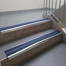 Mill Finish aluminium stair nosing fitted along two concrete steps in an office stairwell, with twin Blue anti-slip inserts running the full width of each step