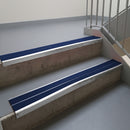 Mill Finish aluminium stair nosing fitted along two concrete steps in an office stairwell, with twin Dark Blue anti-slip inserts running the full width of each step