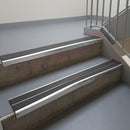 Mill Finish aluminium stair nosing fitted along two concrete steps in an office stairwell, with twin Dark Grey anti-slip inserts running the full width of each step