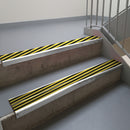 Mill Finish aluminium stair nosing fitted along two concrete steps in an office stairwell, with twin Hazard black and yellow anti-slip inserts running the full width of each step