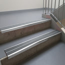 Mill Finish aluminium stair nosing fitted along two concrete steps in an office stairwell, with twin Mid Grey anti-slip inserts running the full width of each step