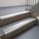 Mill Finish aluminium stair nosing fitted along two concrete steps in an office stairwell, with twin Oyster anti-slip inserts running the full width of each step