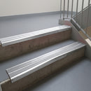Mill Finish aluminium stair nosing fitted along two concrete steps in an office stairwell, with twin Polar Grey anti-slip inserts running the full width of each step