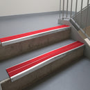 Mill Finish aluminium stair nosing fitted along two concrete steps in an office stairwell, with twin Red anti-slip inserts running the full width of each step